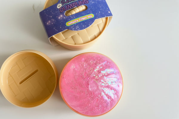 Pink glittery slime in a container with a 'Gushy Dumpling' packaging on a white background

